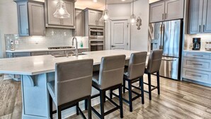 A modern kitchen with a central island, bar stools, stainless steel appliances, and pendant lighting.
