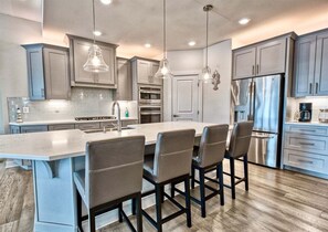 A modern kitchen with a central island, bar stools, stainless steel appliances, and pendant lighting.