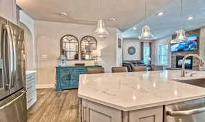 A modern kitchen with a marble island, stainless steel appliances, and a dining area with a TV.