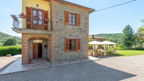 A two-story stone house with a balcony, a covered outdoor seating area, and a gravel driveway.