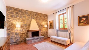 A cozy room with a stone wall, a fireplace, a bench, and a window with curtains.