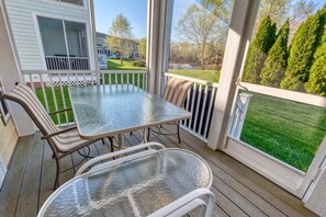 A covered outdoor patio with a table and chairs, a view of a house, and a well-maintained lawn.