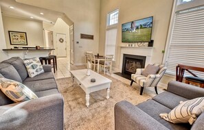 A living room with a fireplace, a television mounted above it, and a dining area with chairs and a table.