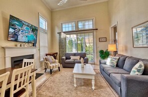 A living room with a fireplace, a television, a sofa, a coffee table, and a dining area. - Bayside * 4 BR Luxury House (Selbyville)
