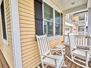 A porch with white rocking chairs and a yellow house.