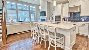 A modern kitchen with a large island, bar stools, white cabinetry, and a fireplace.