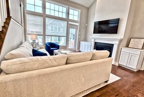 A living room with a beige sofa, a blue chair, a fireplace, and a TV mounted on the wall.