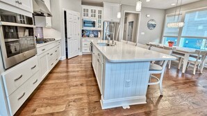 A modern kitchen with white cabinetry, a central island, and a dining area with a large window.