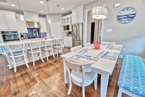 A modern kitchen with white cabinetry, a central island with bar stools, a dining table with a placemat, and a clock on the wall.