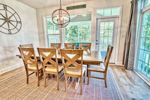 A dining area with a large wooden table and chairs, a hanging light fixture, and a compass wall decoration. - Coastal Club * 4BR Lewes Beach Home (Lewes)
