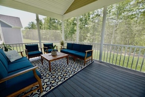 Un patio cubierto con terraza de madera, dos sofás azules, una mesita y una alfombra estampada.