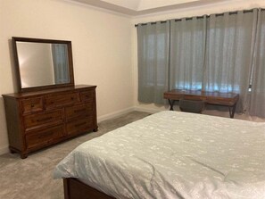 Un dormitorio con cama, cómoda, escritorio y ventana con cortinas.