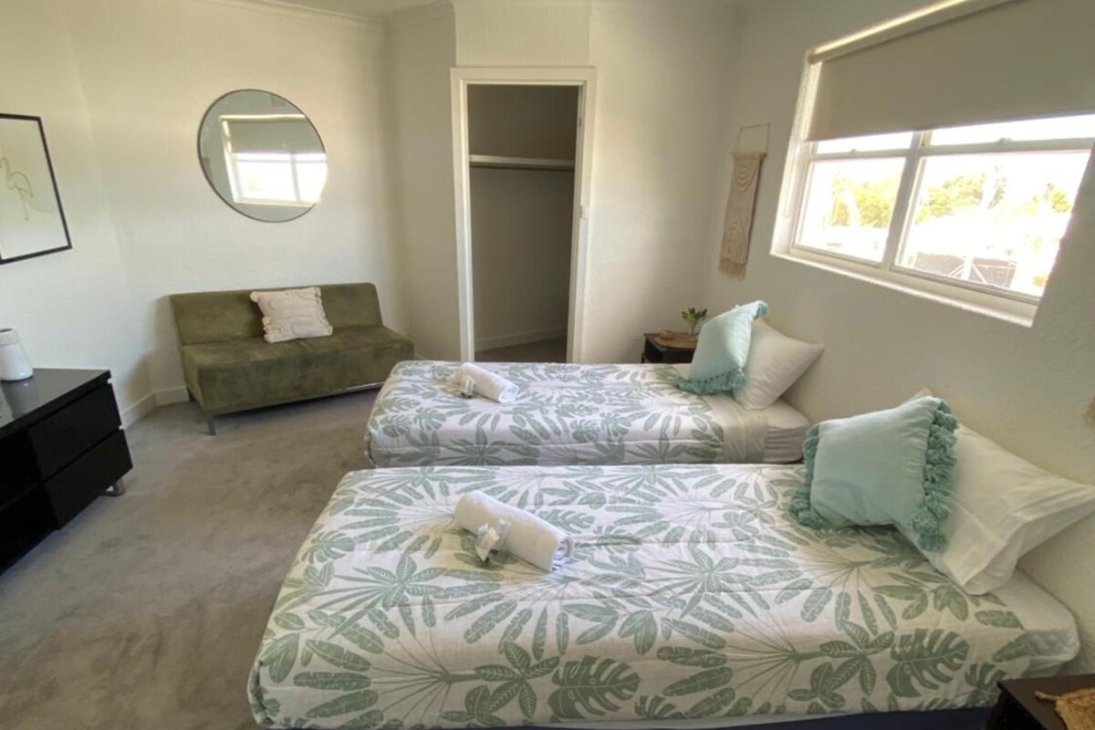 Quarto com duas camas, um guarda-roupa, uma janela e um espelho.