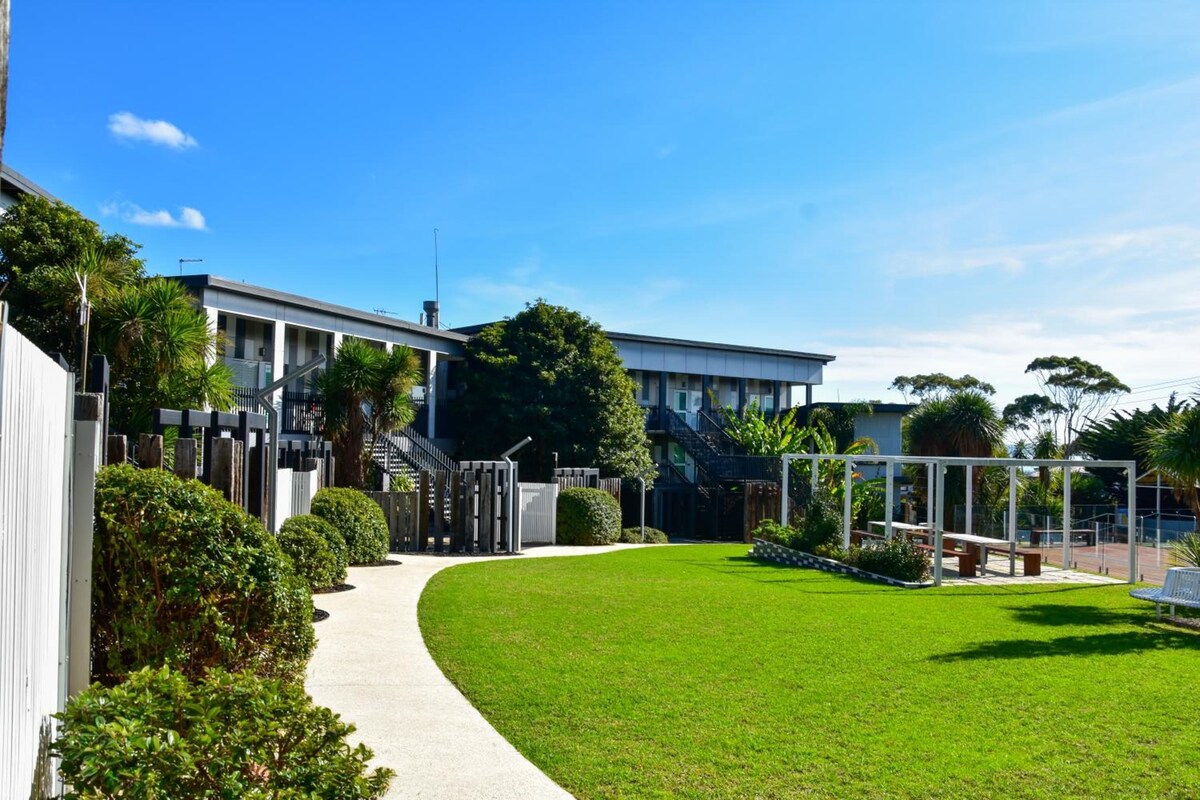 A modern building with a flat roof, surrounded by a well-maintained lawn and a gated entrance.