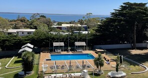 Una piscina con tumbonas y sombrillas, rodeada de árboles y edificios.