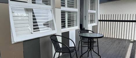 A balcony with a table and chairs, white shutters, and a metal fence.