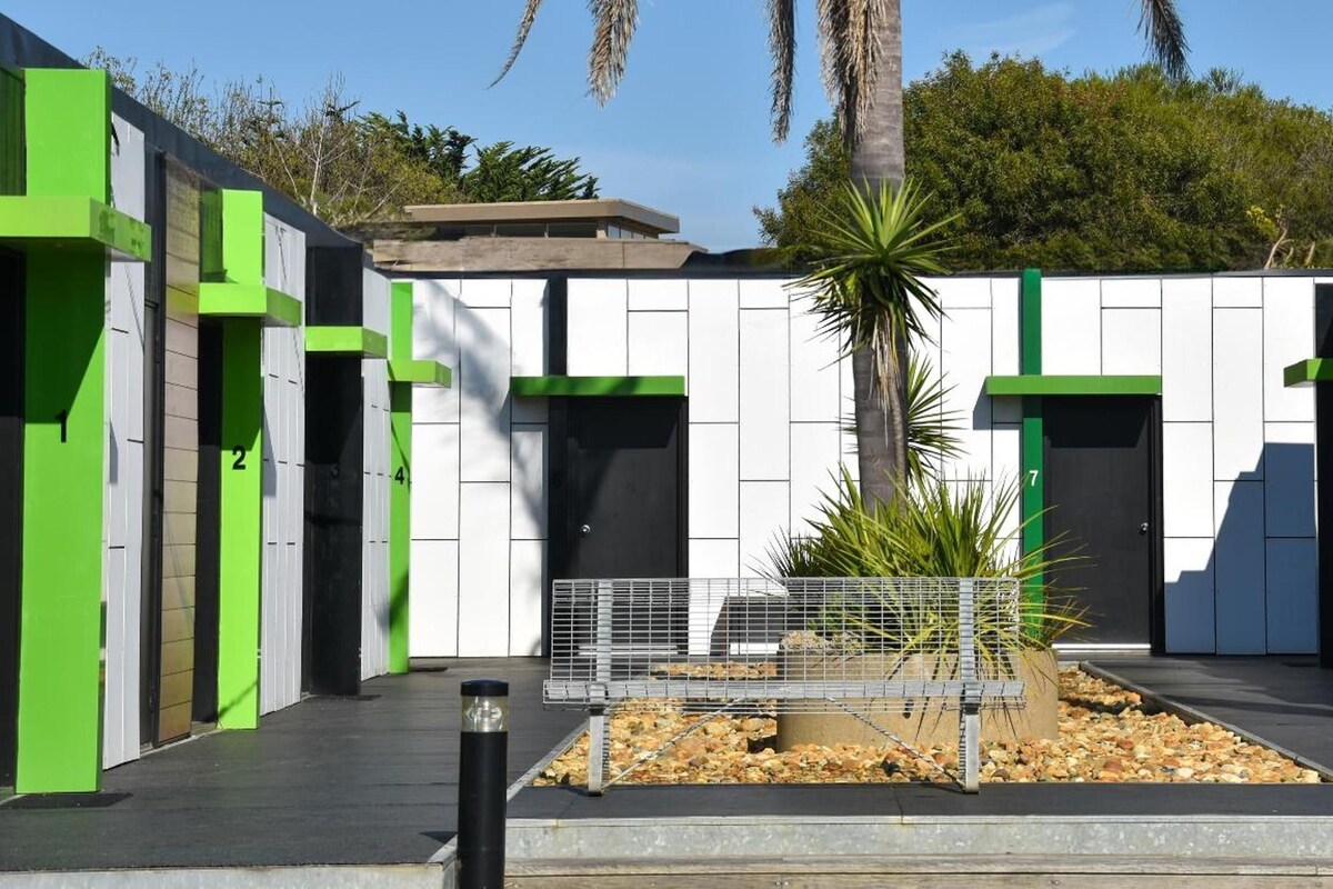 A building with numbered doors, a central planter with a palm tree, and a metal fence.