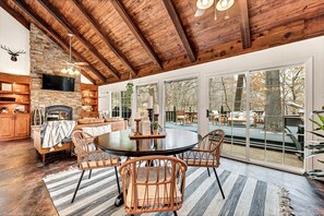 A spacious living room with a stone fireplace, wooden ceiling beams, and large sliding glass doors leading to an outdoor patio. - LOST CAVE COTTAGE. Easy boat parking, BoHo decor, tons of deck space, and a CAVE (Garfield)