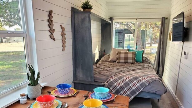 A cozy interior with a wooden dining table set for a meal, a comfortable bed with a plaid blanket, and a large window offering a view of the outdoors. - Dog friendly! - #11 is 1 of 3 containers now dog friendly! (Blanco County)
