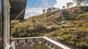 A wooden deck with wicker chairs overlooking a hilly landscape with sparse vegetation and a clear sky. - 3 bedroom nice home in Oppdal (Oppdal)