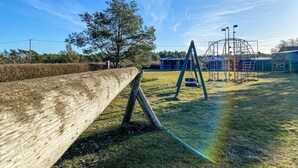 A playground with swings and a slide, surrounded by a wooden fence and trees. - Nice home in Visby with WiFi (Visby)
