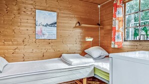 A wooden cabin room with two beds, a small table, a wall-mounted shelf, and a window with a view of trees. - Nice home in Visby with WiFi (Visby)