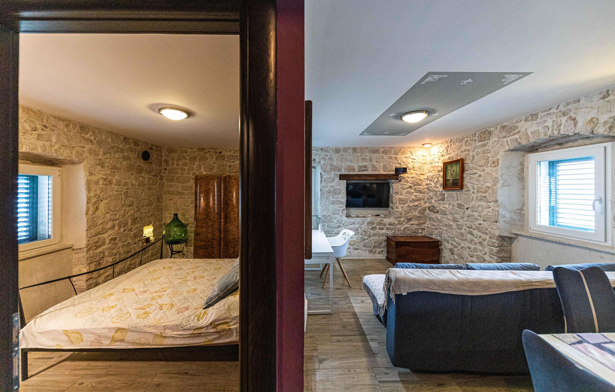 Une pièce avec un mur en pierre, un lit, un canapé, une petite table et un téléviseur.