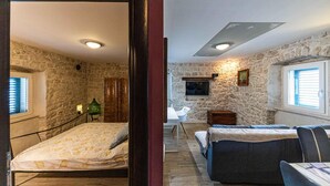 Una habitación con pared de piedra, una cama, un sofá, una mesita y un televisor.