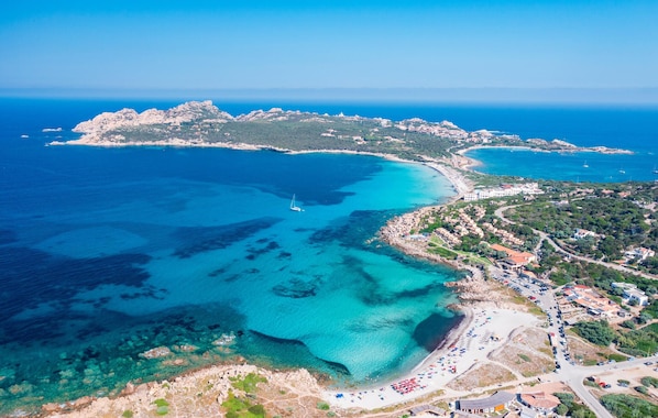 An aerial view of a coastal town with clear blue waters, a rocky coastline, and a mix of residential and commercial buildings.