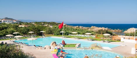 Piscina com espreguiçadeiras e guarda-sóis, rodeada por vegetação e vista para o mar.