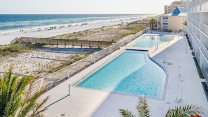 Ein Poolbereich mit Blick auf einen Strand, eine Holzterrasse und ein Gebäude mit Balkonen.