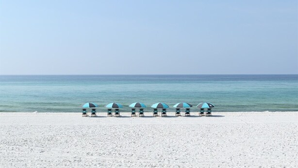 Ein Strand mit fünf Strandsonnenschirmen, die in einer Reihe zum Meer ausgerichtet sind.