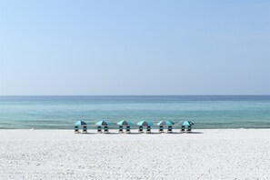 Una playa con cinco sombrillas de playa alineadas, mirando hacia el océano.