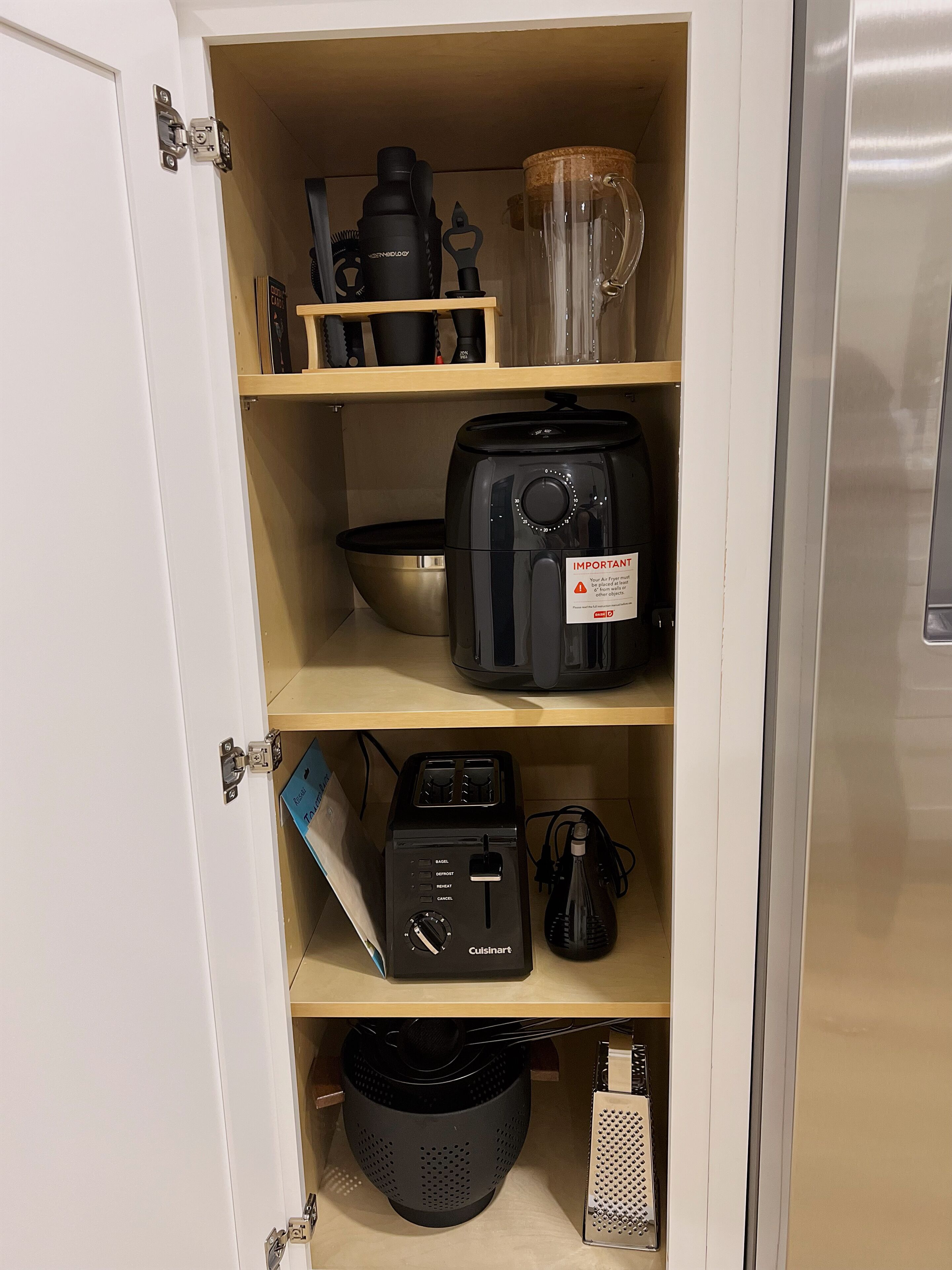 A kitchen with a Cuisinart toaster, a coffee maker, a kettle, and a kettle on the shelf.