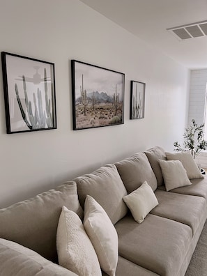 A living room with a beige sofa, three framed desert landscape paintings, and a small plant on a side table.