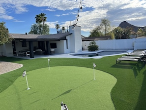 A backyard with a pool, artificial grass, and lounge chairs.