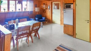 Ein gemütliches Blockhauszimmer mit Holzvertäfelung, einem Esstisch mit Stühlen, einem blauen Sofa und einer Küchenzeile mit Mikrowelle und Kühlschrank.