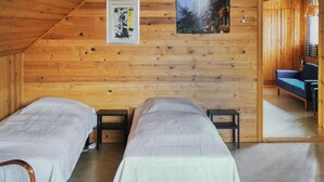 Ein gemütliches Zimmer mit zwei Einzelbetten, Holzwänden, einem kleinen Tisch und einer Couch.