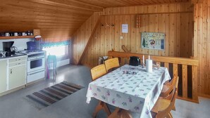 Eine gemütliche, rustikale Küche mit Holzwänden, einem Esstisch mit Blumenmuster und einem kleinen Essbereich mit Stühlen.