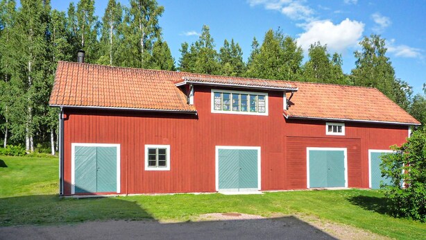 Ein rotes Bauernhaus mit einem Ziegeldach, zwei grünen Türen und einem Fenster mit weißem Rahmen.
