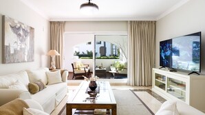 Una sala de estar moderna con sofá, mesa de centro, televisor y vistas al exterior.