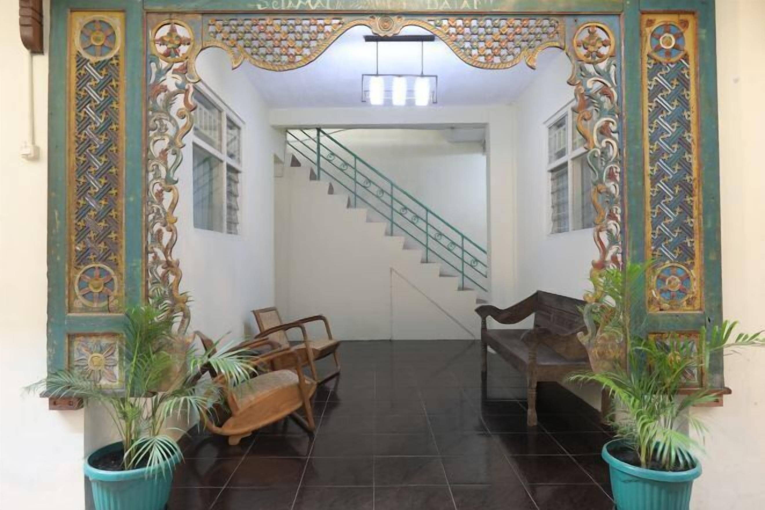 A lobby with a staircase, wooden chairs, and potted plants.