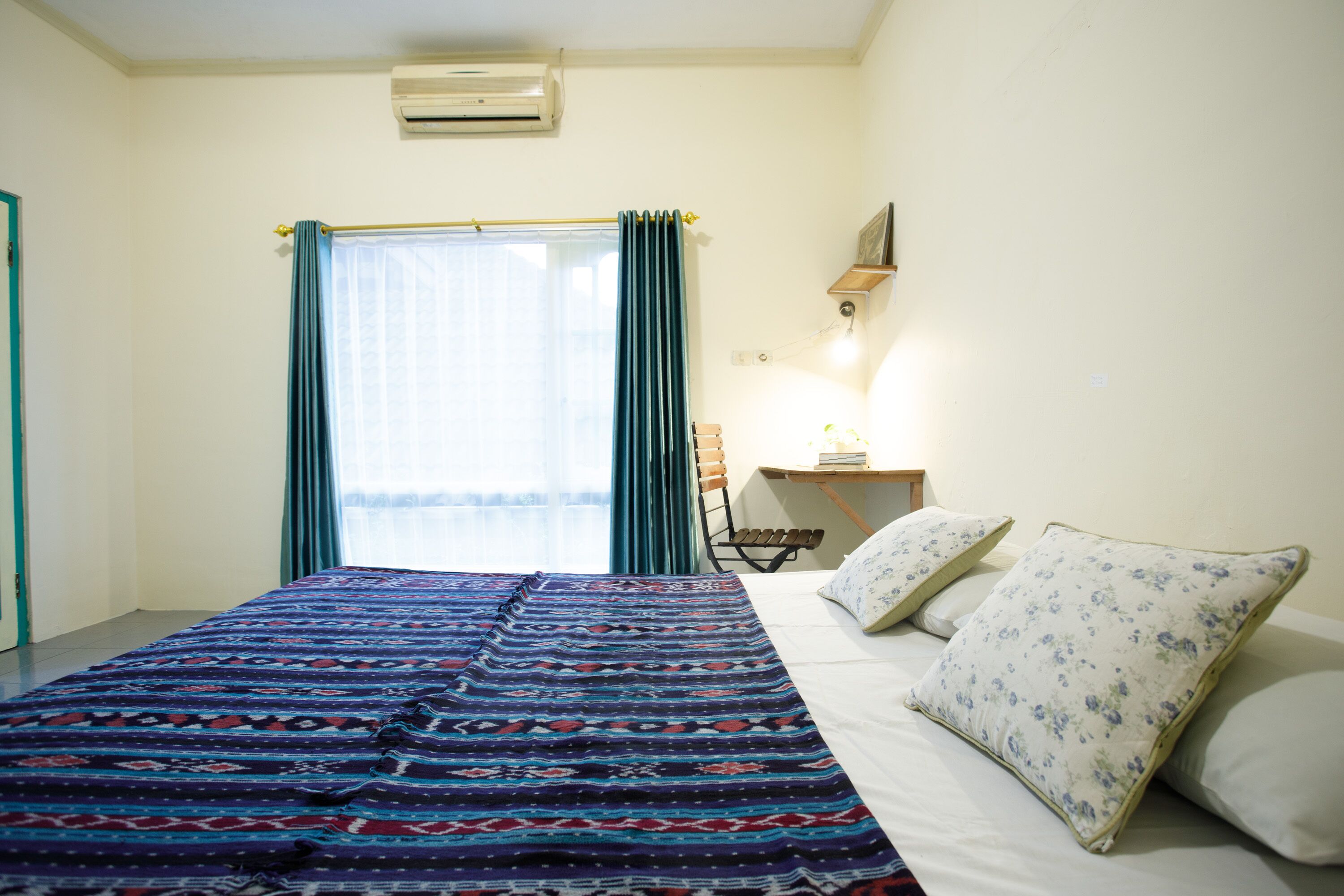 A bedroom with a bed, a desk, a chair, and a window with curtains.