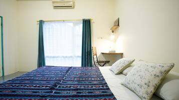 A bedroom with a bed, a desk, a chair, and a window with curtains.