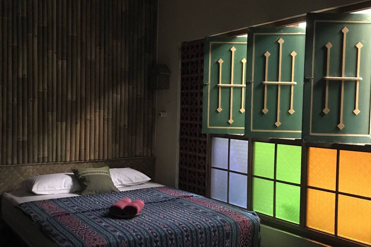 Une pièce avec un lit, une fenêtre aux vitres vertes et jaunes, et un climatiseur fixé au mur.