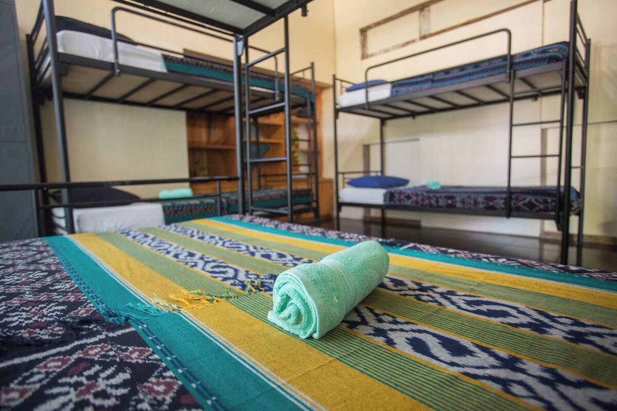 Une chambre avec des lits superposés, une couverture à motifs et une serviette enroulée posée sur le lit.