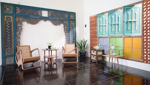 A room with a tiled floor, two wicker chairs, a small table, a potted plant, and a decorative wall with geometric patterns. - Rumah Kalpataru (Yogyakarta)