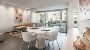 A modern living room with a round dining table, white chairs, a sofa, and a large window offering a view of the outside. - Jardines - Tisaya 0.2,  Garden View  (Arona)