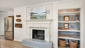 Een keuken met een witte bakstenen open haard, een roestvrijstalen koelkast en planken met manden en decoratieve objecten.