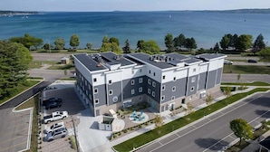 A multi-story building with a parking lot, a swimming pool, and a view of the water. - 🌆 539 Bay St Downtown Lakeview Condo | 102W - Waterfront, Free Parking, Moments from festival grounds (Traverse City)